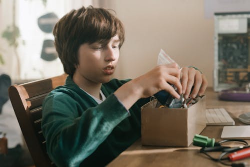 Free Young boy focused on exploring electronics components at a computer desk, embodying tech enthusiasm. Stock Photo